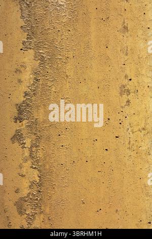 Thin paint layer on rustic concrete displays corrugated surface with scattered holes. Uneven textures create mountain like range in shades of orange. Stock Photo