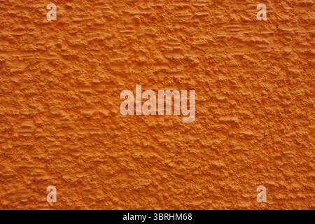 Textured stucco wall surface coated in vivid orange paint features parallel rows of ridges resembling small mountains stretched across barren plain. Stock Photo