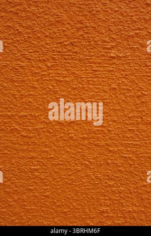 Vivid orange stuccoed wall features multiple linear rows of small parallel surface ridges which resemble an ariel photograph of mountainous terrain. Stock Photo