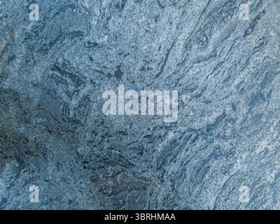 Cut slab from coarse-grained granite features multiple swirling patterns resembling flowing murky waters that can be seen on an ocean beach. Stock Photo