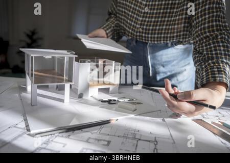 House model on Buleprint construction drawing and drawing equipment stationary Architect analyzing house model house modern in hand Architect Design C Stock Photo