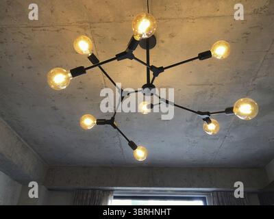 Light bulbs with warm lighting in stylish chandelier with exposed wiring on gray concrete ceiling, interior in retro loft design Stock Photo