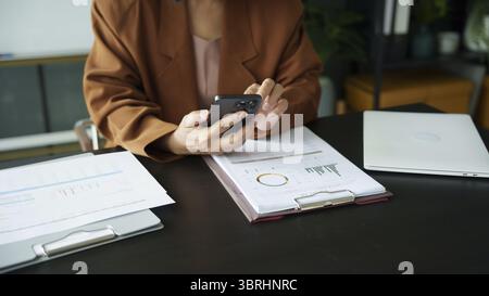 Middle age Asian woman holding cell telephone. senior business woman with smart phone elderly woman using smartphone in office with technology Stock Photo