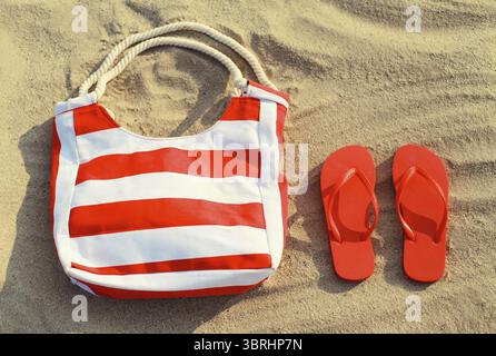 Summer vacation, accessories - red striped bag with flip flops lying on the sand on the beach, top view Stock Photo