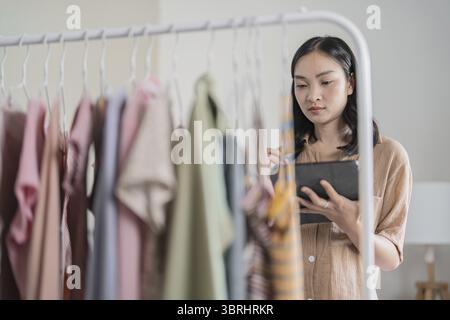 Asian Woman holding digital tablet in small cloth shop Online store selling or e-commerce Stock Photo