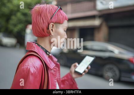 Traveler Gen z girl leather fashion with punk Asian woman tourist in city street searching location in map application online smart phone using GPS na Stock Photo