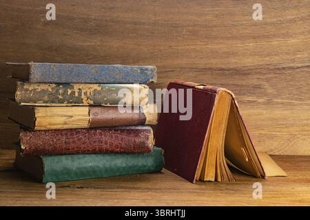 Side view stack of old torn hardcover books on wooden table. Old grungy books on wooden baclground Stock Photo