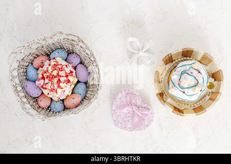 Sweet Easter cakes and colorful Easter eggs in the wooden baskets with gift boxes on the white background. Top view Stock Photo