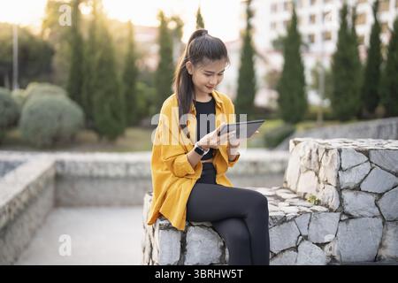 Smiling young Asian woman using digital tablet in urban city Stock Photo