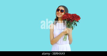 Portrait of beautiful smiling woman with bouquet of red rose flowers in heart shaped sunglasses on blue background Stock Photo