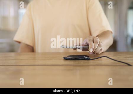 Charging mobile phone battery with wireless charging device in the table. Smartphone charging on a charging pad. Mobile phone near wireless charger Mo Stock Photo
