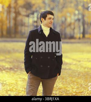 Portrait of elegant caucasian young man in black coat outdoors in autumn park with yellow leaves Stock Photo