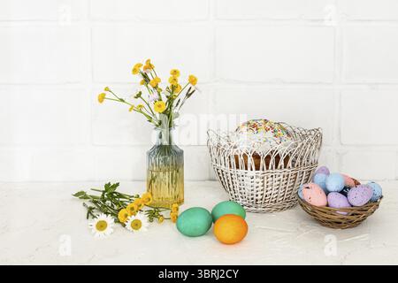 Easter cake and colored Easter eggs in the wicker baskets with yellow Ranunculus asiaticus in the glass vase Stock Photo