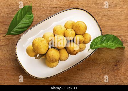 Top view of a bunch of ripe Long kong, Lansium domesticum, Longkong, Langsat, Longgong in brown ceramic tray with dark edge on wooden table Stock Photo