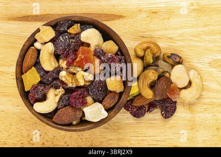 Top view of various dried mixed fruits and nuts in wooden bowl and pile on wooden board Stock Photo
