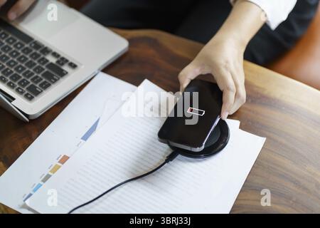Charging mobile phone battery with wireless charging device in the table. Smartphone charging on a charging pad. Mobile phone near wireless charger Mo Stock Photo