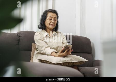 Middle age Asian woman holding cell telephone. senior woman with smart phone. elderly woman using smartphone at home with technology concept Stock Photo