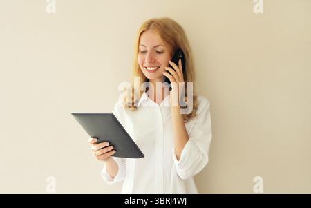 Portrait of caucasian young woman employee with digital tablet computer or folder with documents and calling on mobile phone in office Stock Photo