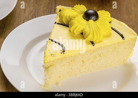 High angle view closeup slice of delicious homemade sponge cake garnished with cream flower in white ceramic dish on wooden table Stock Photo