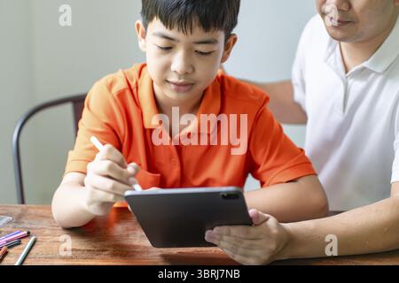 Asian father and son using tablet teaching son to draw playing with digital tablet at desk fatherhood concept Stock Photo