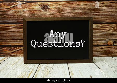 Any Questions? text written on chalkboard standing on wooden background Stock Photo