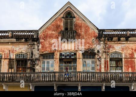 a local lady walks along an upper storey stone balcony on a beautiful but rundown colonial building in sao tome city centre Stock Photo