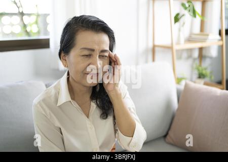 Middle age Asian woman touching forehead having headache suffering from migraine. mature asian woman feeling sick or depression Stock Photo
