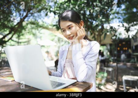 Beautiful confident freelancer asian young woman working with laptop Hands typing keyboard. digital nomad working remotely from outdoor eco cafe Workp Stock Photo