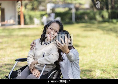 Asian senior woman in wheelchair with happy daughter taking selfie photo with smartphone Stock Photo