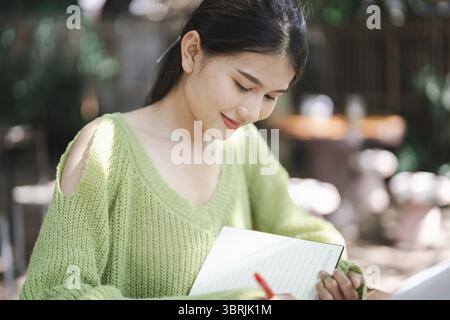 Beautiful asian young woman students studying writing on notebook, working on laptop computer at outdoor eco cafe Academic Research With Workplace on Stock Photo