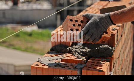 Bricklayer building wall with red bricks. Close-up of a construction worker laying red bricks with mortar to build a wall on a sunny day at a job site Stock Photo