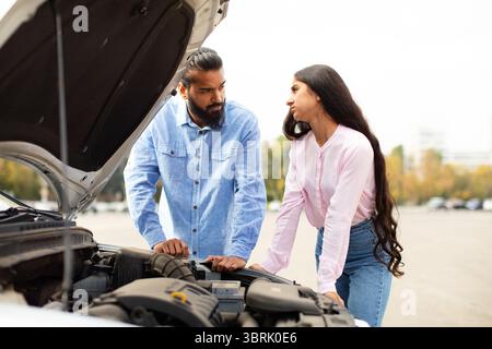 Indian couple leaning on broken cars hood, having serious conversation Stock Photo