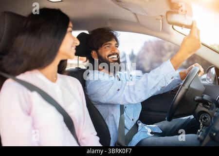 Smiling Indian man adjusting rear view mirror in car while girlfriend smiling Stock Photo