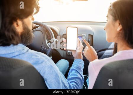 Indian couple using smartphone with blank white screen in car, discussing app Stock Photo