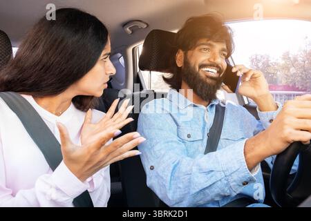 Frustrated Indian woman gesturing while man talks on phone while driving Stock Photo