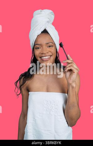 Young woman holding a toothbrush and smiling with towel on head and body after shower on pink background Stock Photo
