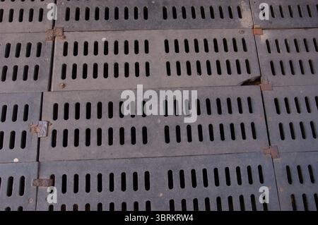 A large rusty metal drain grate field covers the ground, made of many rough, patched-together sections. The weathered, damaged grates create a rugged Stock Photo