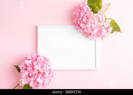 Blank picture frame and hydrangea flowers on pink background. Copy space for text. Top view, flat lay. Stock Photo