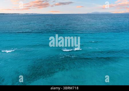 Gentle waves rolling in crystal clear turquoise waters, creating a serene atmosphere beneath a stunning pastel sunset sky Stock Photo