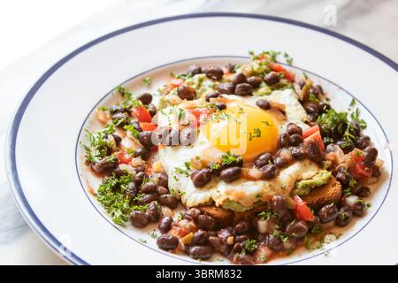 Fried egg on whole wheat toast spread with avocado  and served with black beans and tomato salsa on a blue rimmed plate.  A healthy breakfast special Stock Photo