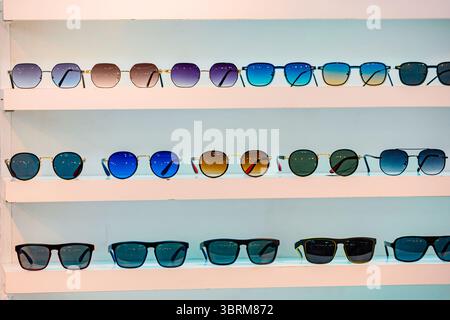 Modern sunglasses in different shapes and colors are neatly arranged on illuminated shelves, ready for customers to choose their perfect pair Stock Photo