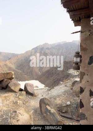 A mountain landscape with rocky terrain and an old lantern hanging from a rustic building. Dry, rugged cliffs stretch into the distance under a clear Stock Photo