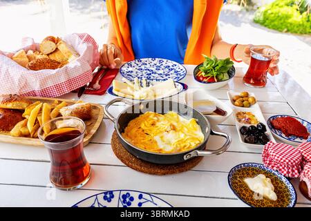 Woman having a rich and delicious turkish breakfast with scrambled eggs, tea, cheese, olives, pastries and various other local delicacies Stock Photo