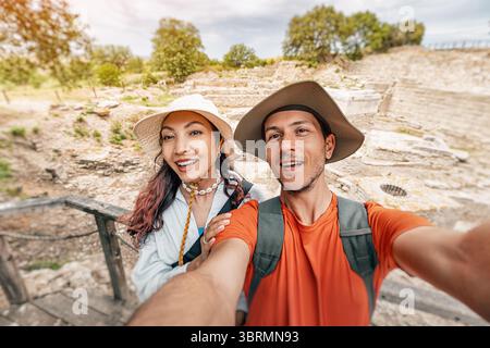 Smiling couple capturing a joyful selfie amidst ancient ruins at an archaeological site, enjoying their travel adventure Stock Photo