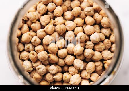 Raw chickpeas in glass jar. Dry beige legumes from top view. Healthy organic protein source. Natural vegan food ingredient. Macro of round pulses. Stock Photo