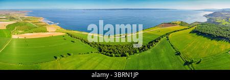 Vast green fields stretch towards the blue sea under a clear sky, creating a picturesque landscape Stock Photo