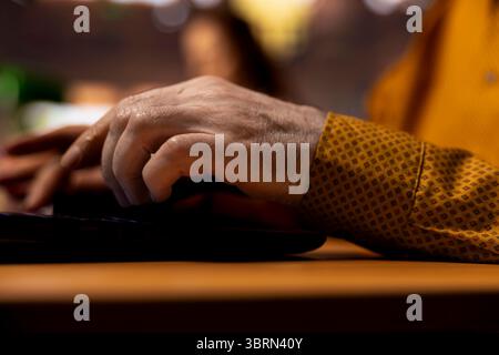 Senior person in a college library working on his thesis under a green lamp, surrounded by books and study materials. Aged student reflecting ambition for learning and achievements. Close up. Stock Photo