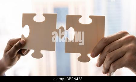 Closeup view of two hands holding pieces of jigsaw puzzle Stock Photo