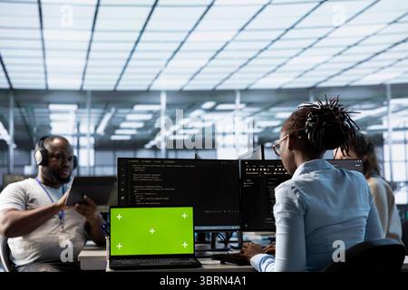 Green screen laptop in data center in front of IT support specialists working together, supervising server rows. Employees overseeing supercomputers using mockup notebook device Stock Photo