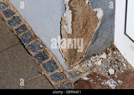 Close-up of a building corner with damaged wall, brick edging, and broken debris on the ground. Stock Photo